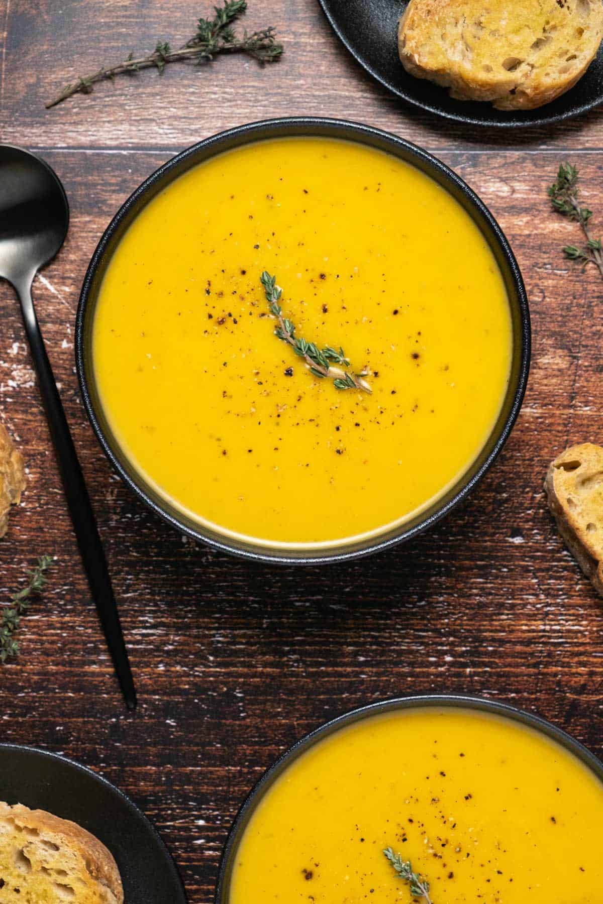 Vegan butternut squash soup topped with black pepper and a sprig of fresh thyme. 