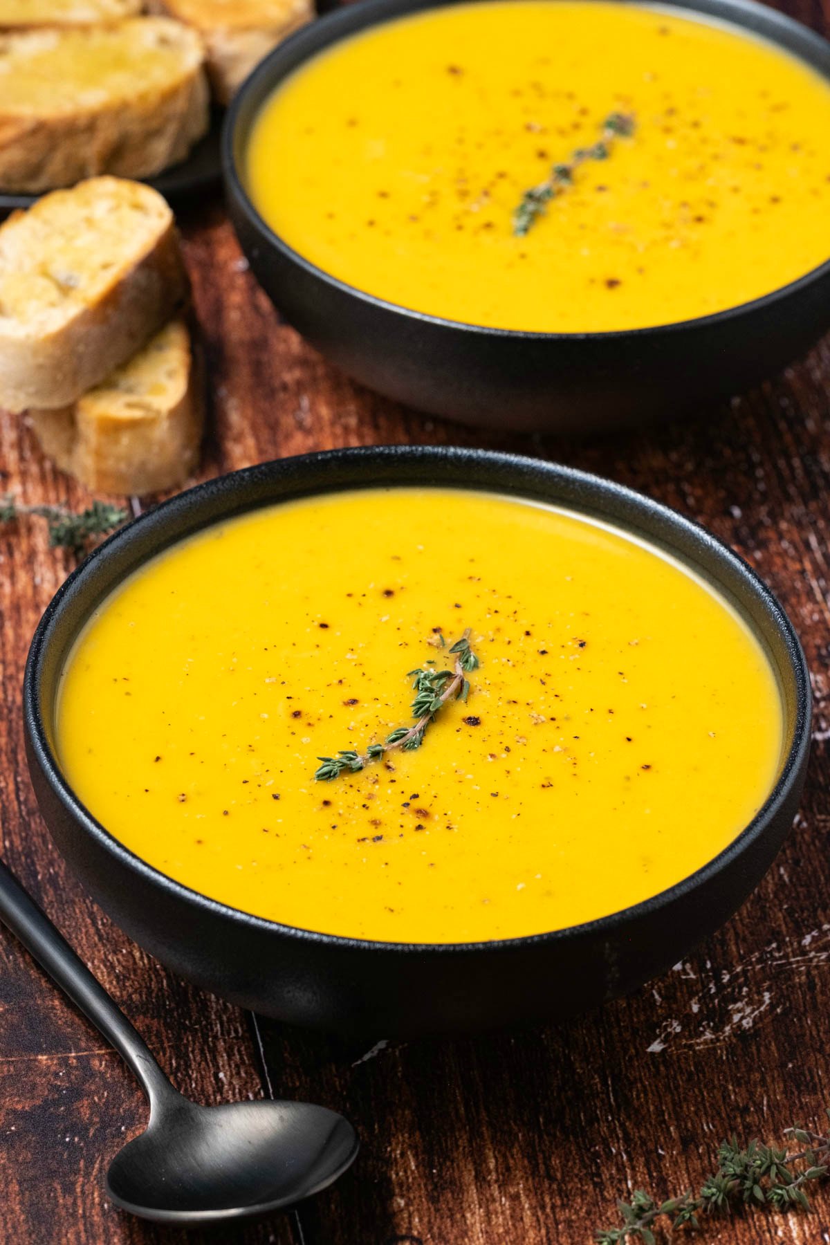 Roasted butternut squash soup with black pepper and thyme in a black bowl. 
