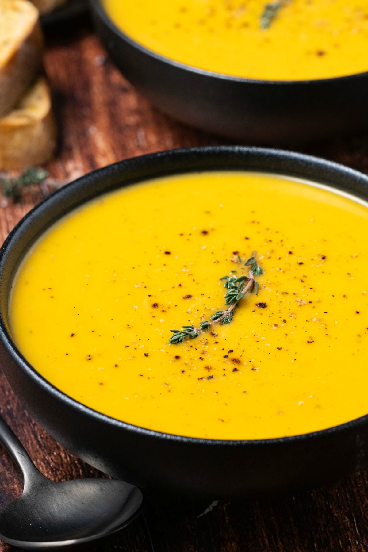 Butternut squash soup in a black bowl with black pepper and fresh thyme. 