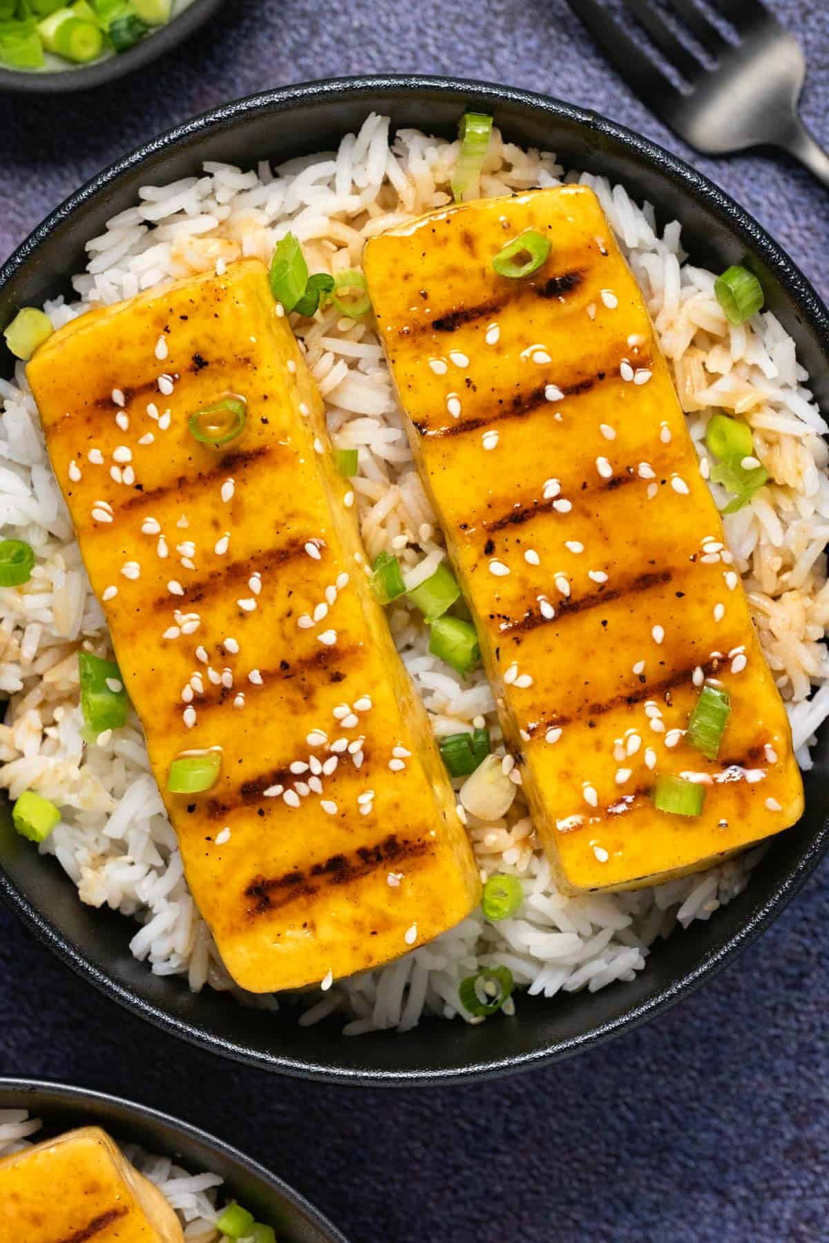 Grilled tofu with rice in a black bowl. 