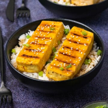 Grilled tofu with rice in a black bowl.