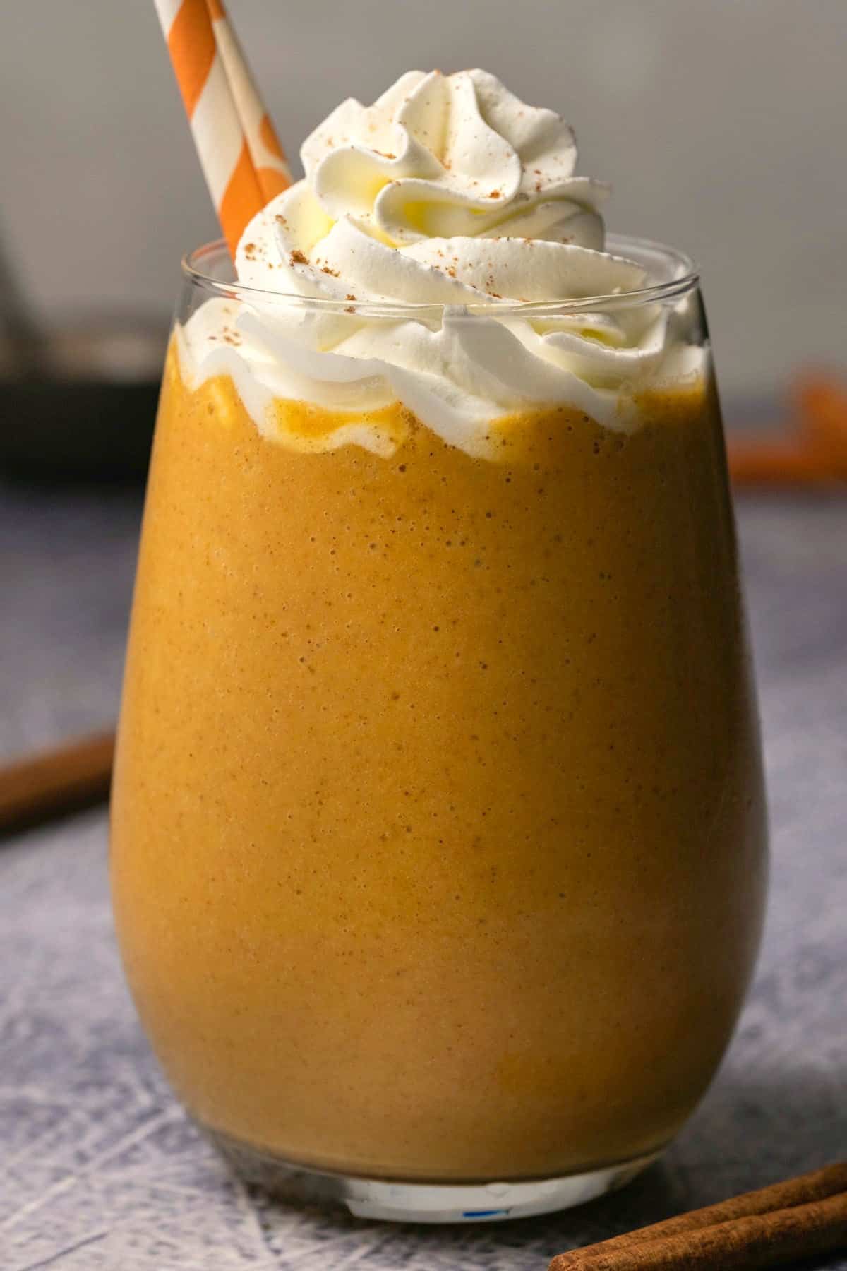 Pumpkin pie smoothie in a glass with whipped cream and pumpkin pie spice. 
