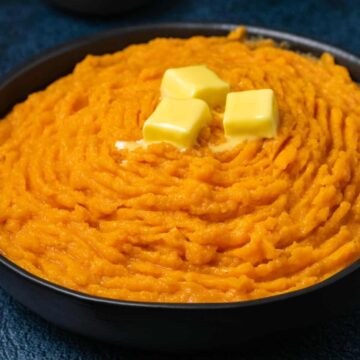 Vegan mashed sweet potatoes topped with butter in a black bowl.