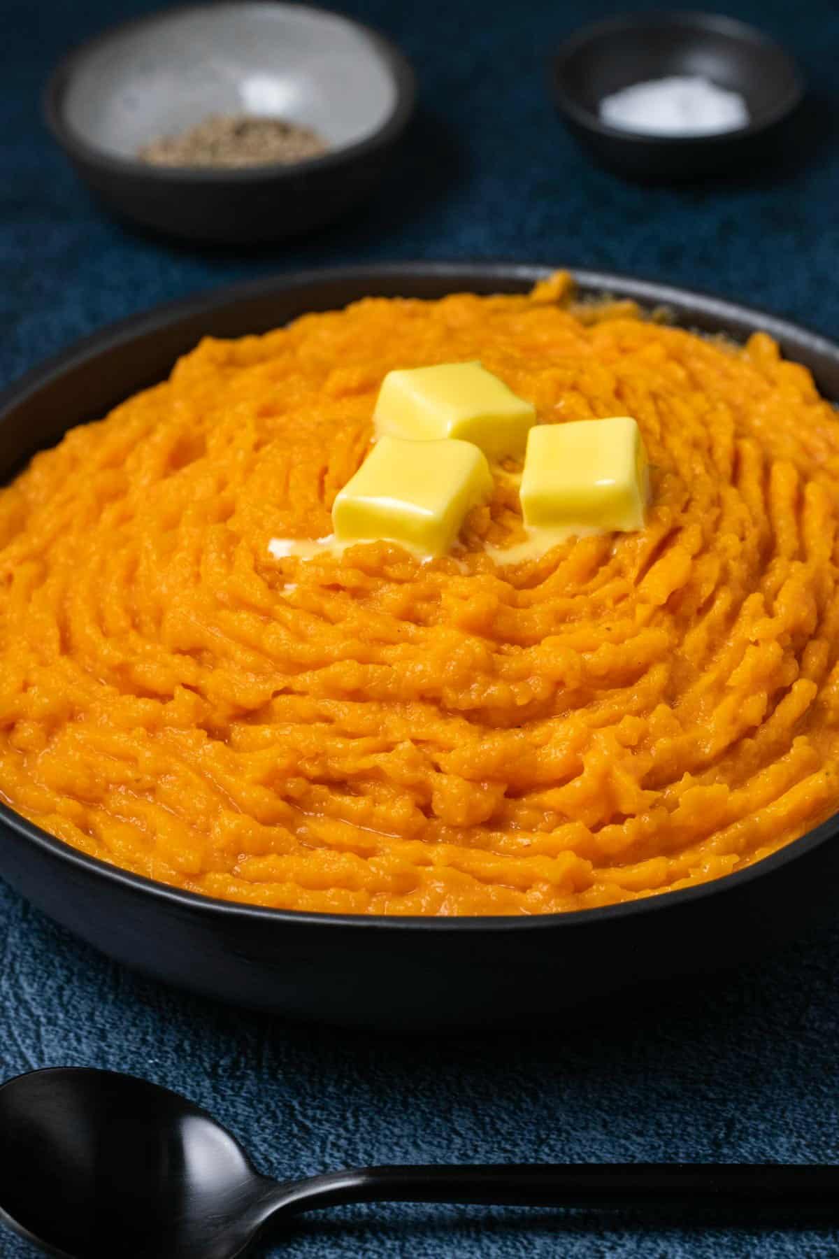Vegan mashed sweet potatoes topped with knobs of vegan butter in a black bowl. 