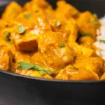 Vegan butter chicken with rice in a black bowl.
