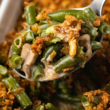 Vegan green bean casserole in a white dish with a serving spoon.