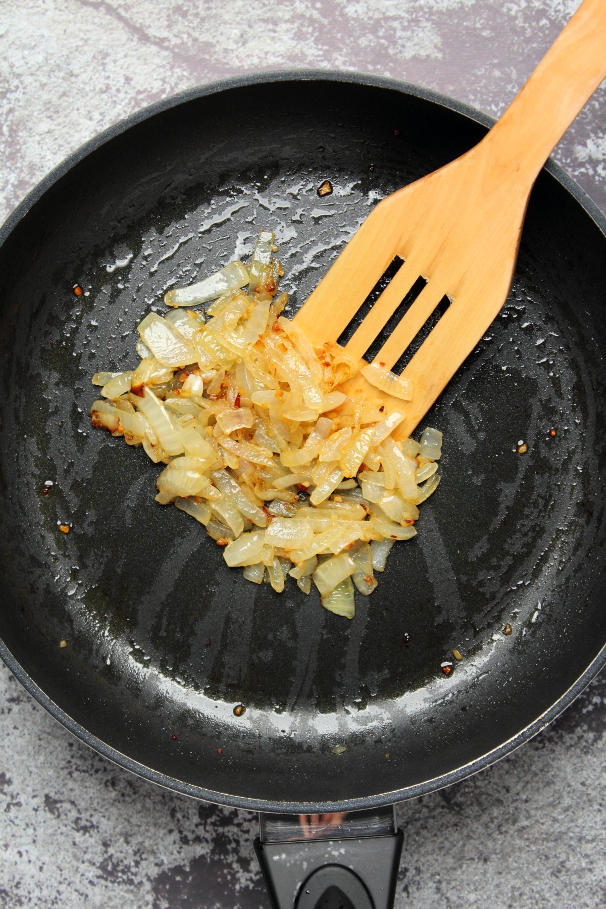 Sautéed onions in a frying pan with a wooden spatula. 