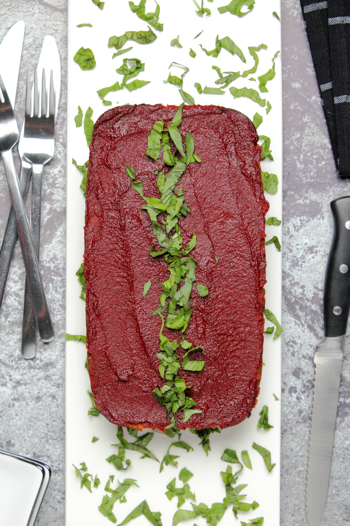 Vegan meatloaf on a white plate with fresh chopped basil.