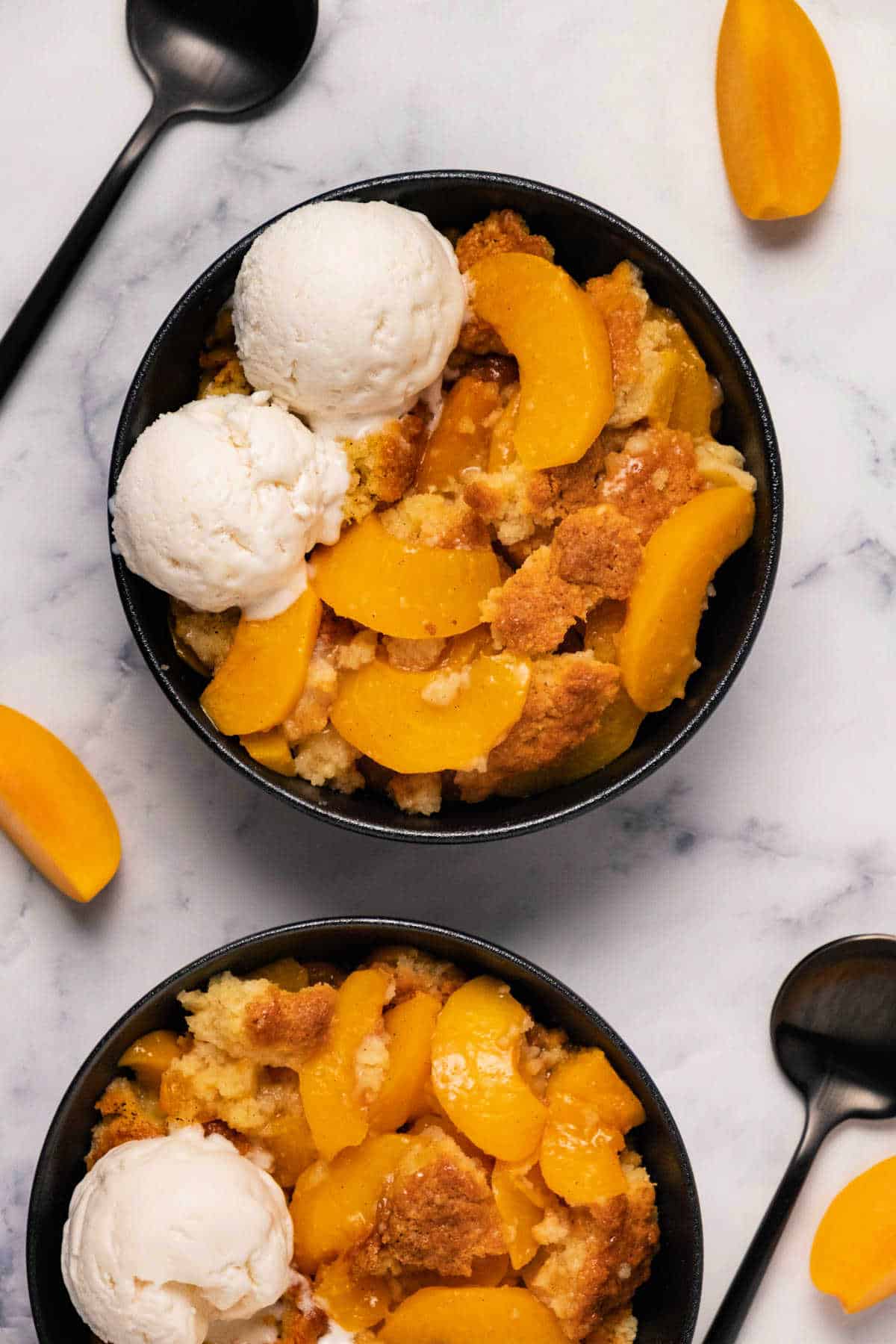 Peach cobbler in a black bowl with ice cream. 