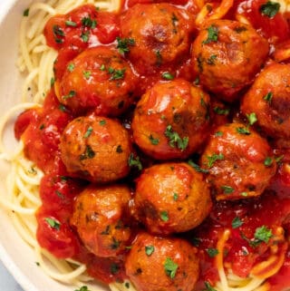 Close up photo of spaghetti, chickpea meatballs and sauce in a white bowl.
