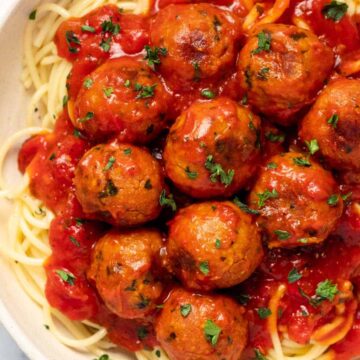 Close up photo of spaghetti, chickpea meatballs and sauce in a white bowl.