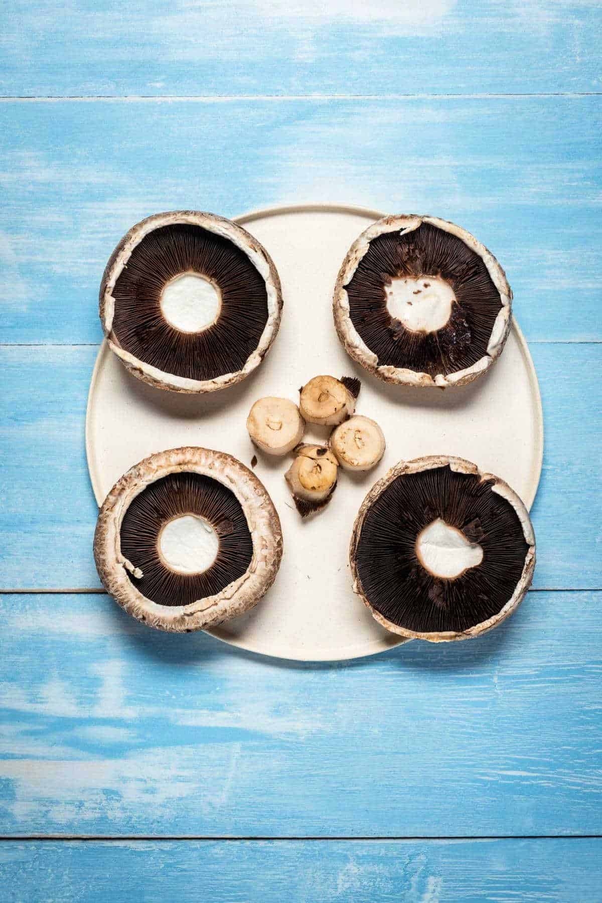 Portobello mushrooms with stems cut off on a white plate.