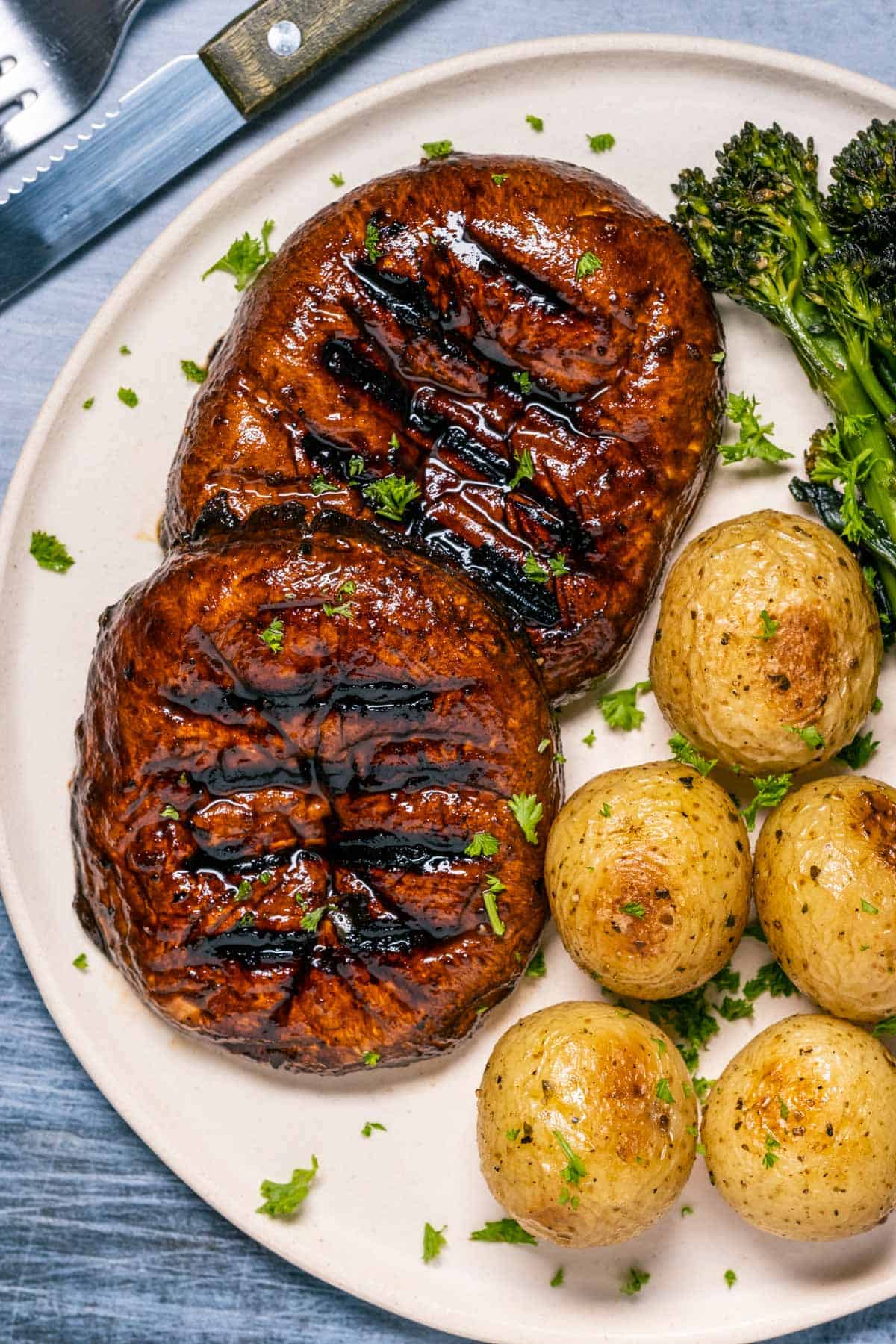 Portobello steaks on a plate with baby potatoes and broccoli.