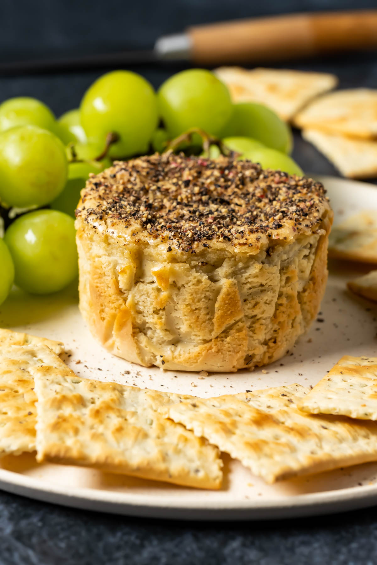 Vegan camembert on a white plate with crackers and grapes.