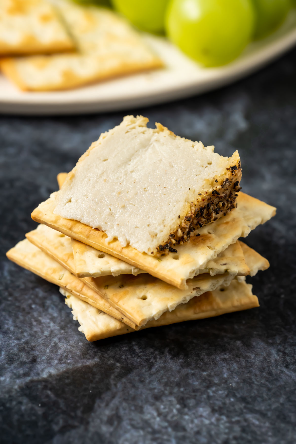 A stack of crackers topped with a thick slice of vegan camembert.