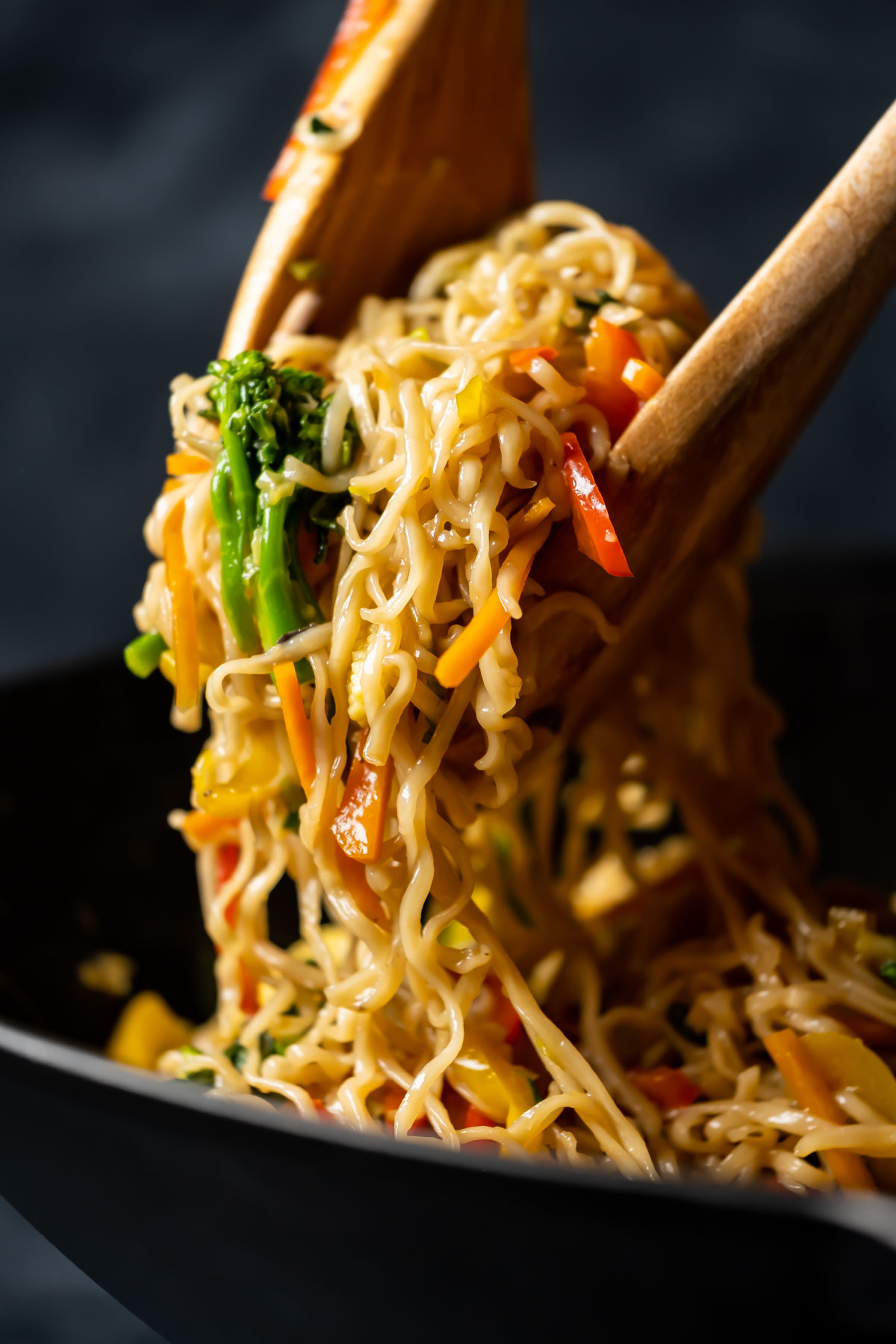 Wooden serving spoons lifting noodles and veggies out of a wok.