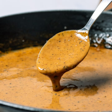 Vegan peppercorn sauce in a black skillet with a spoon.