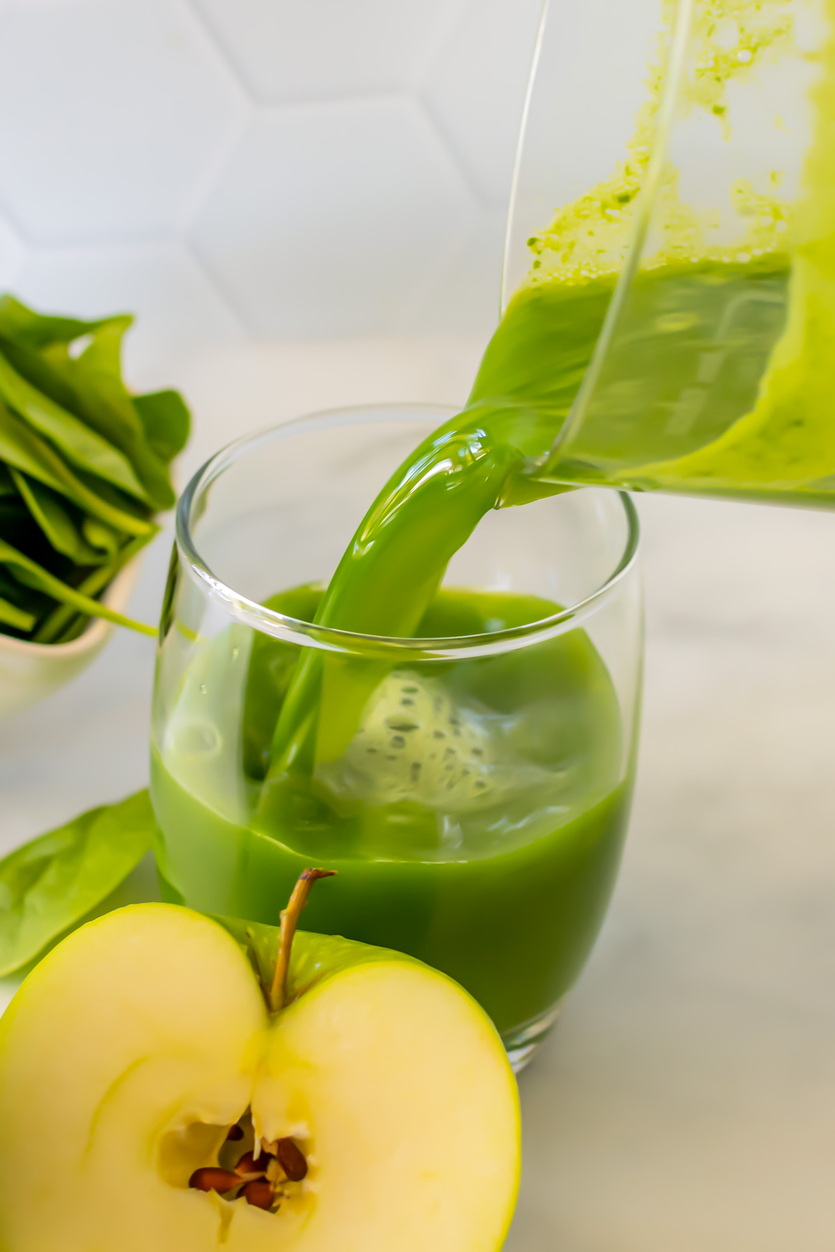 Green juice pouring from a jug into a glass.