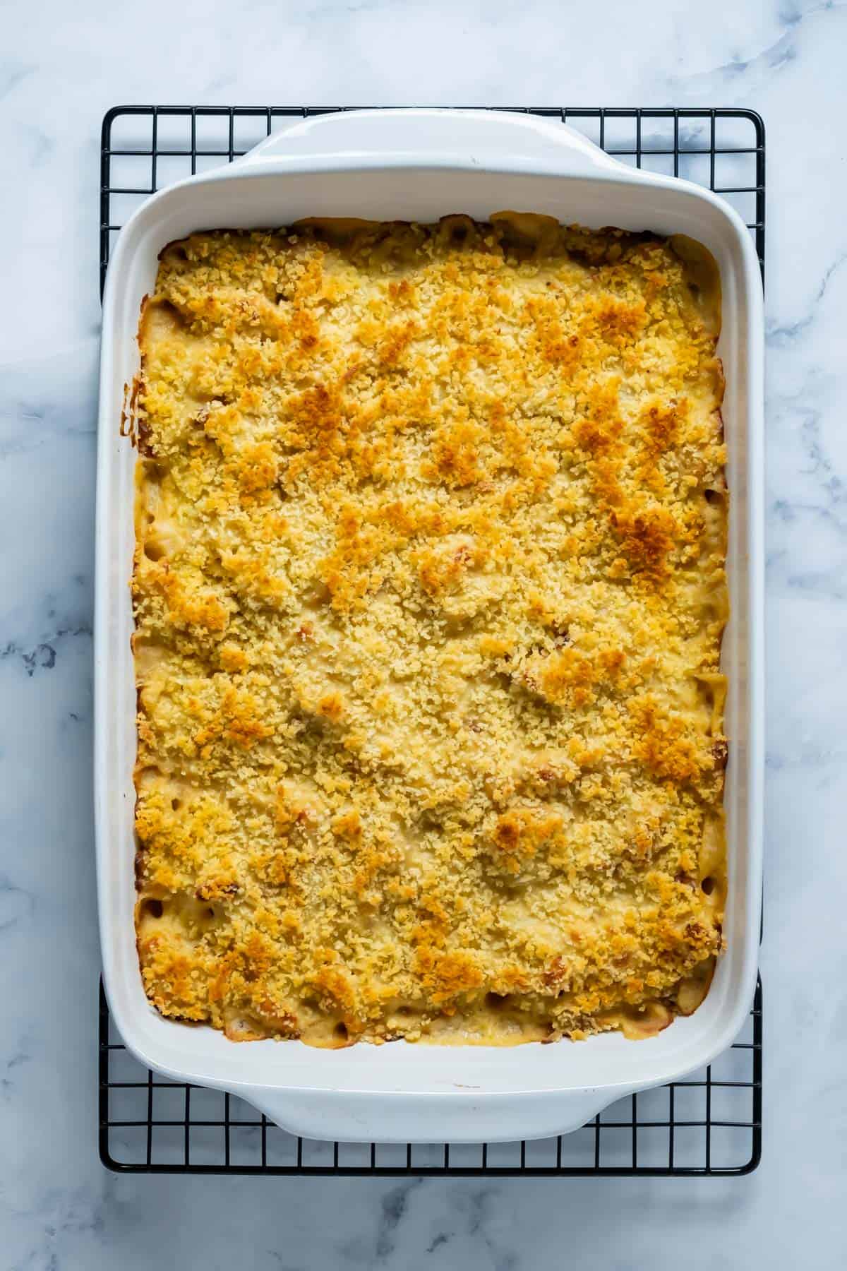 Freshly baked vegan cauliflower cheese in a white baking dish on a wire cooling rack.