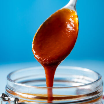 Vegan BBQ sauce drizzling from a spoon into a glass jar.