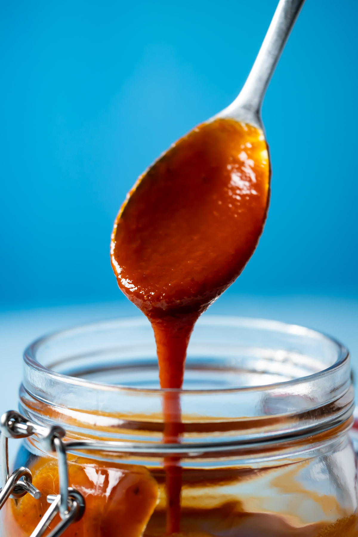 Vegan BBQ sauce drizzling from a spoon into a glass jar. 