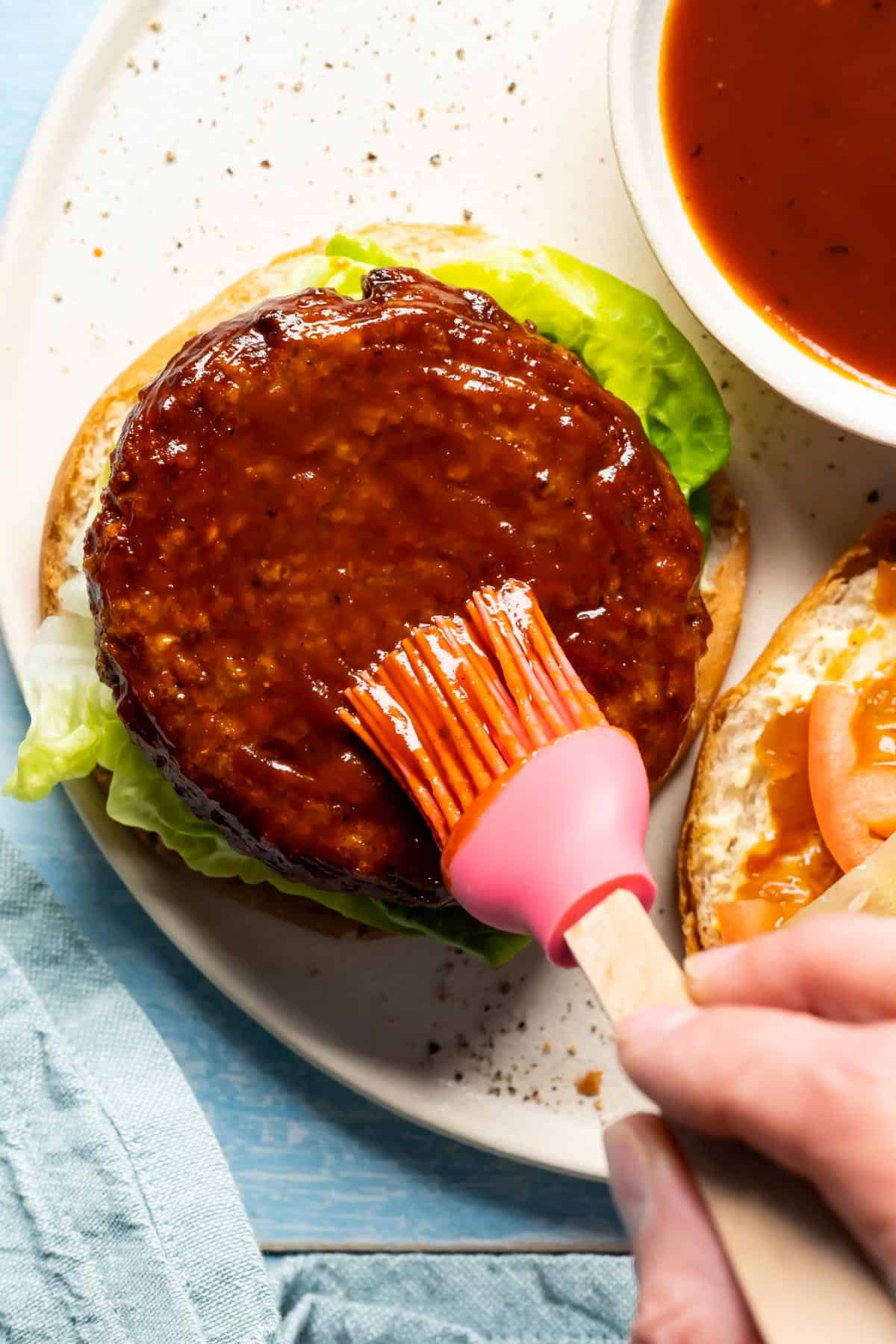 Brushing vegan bbq sauce onto a veggie burger.