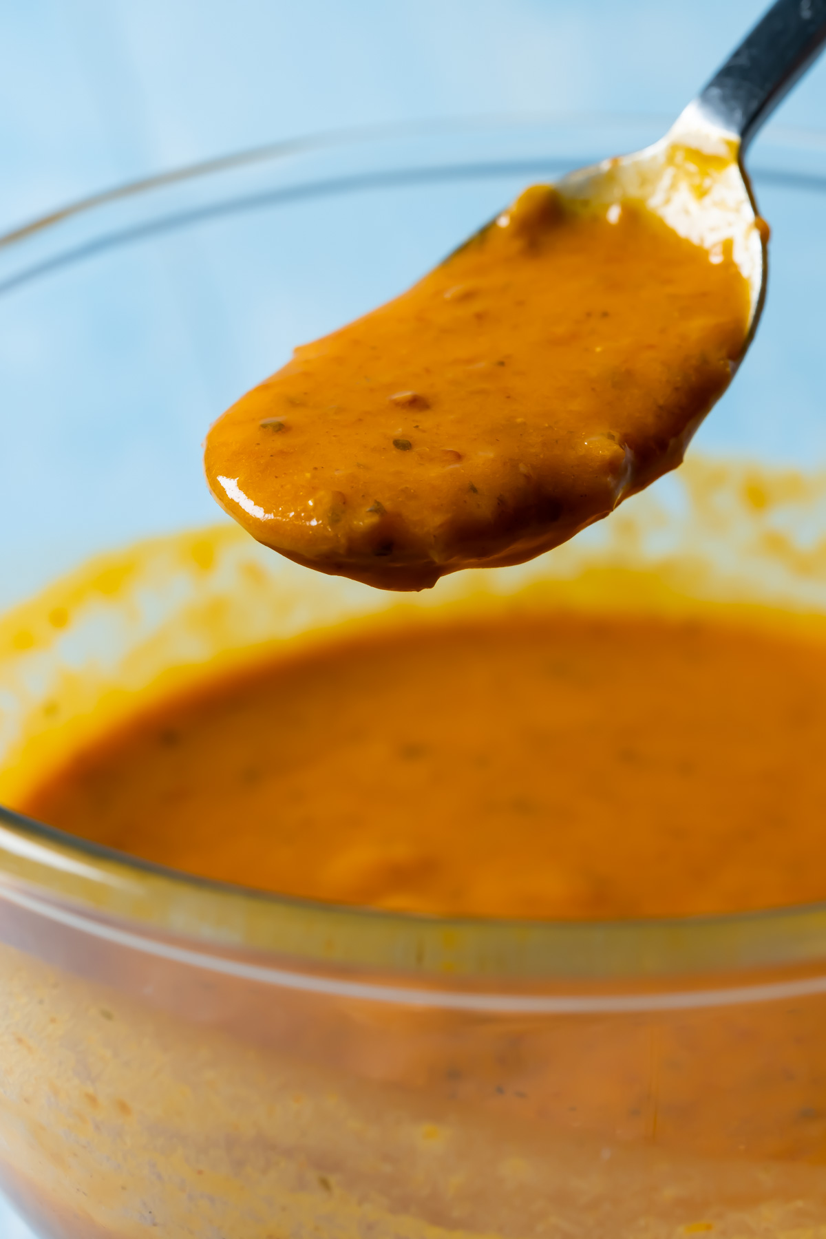 Vegan buffalo sauce in a glass bowl with a spoon.