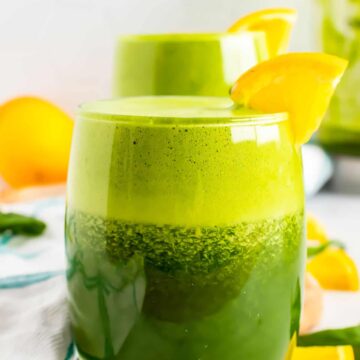 Blended green juice in glasses with orange slices.