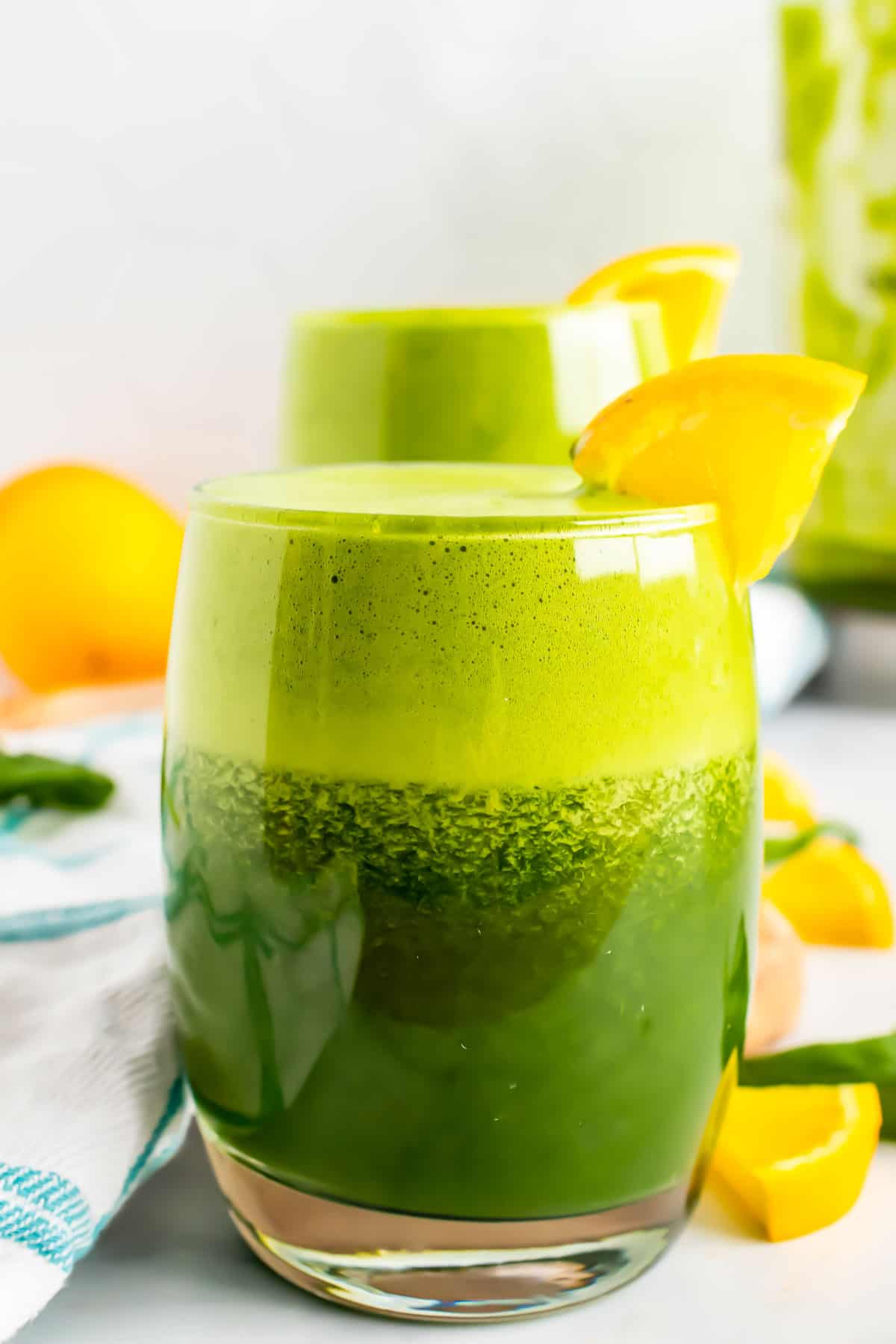Blended green juice in glasses with orange slices.