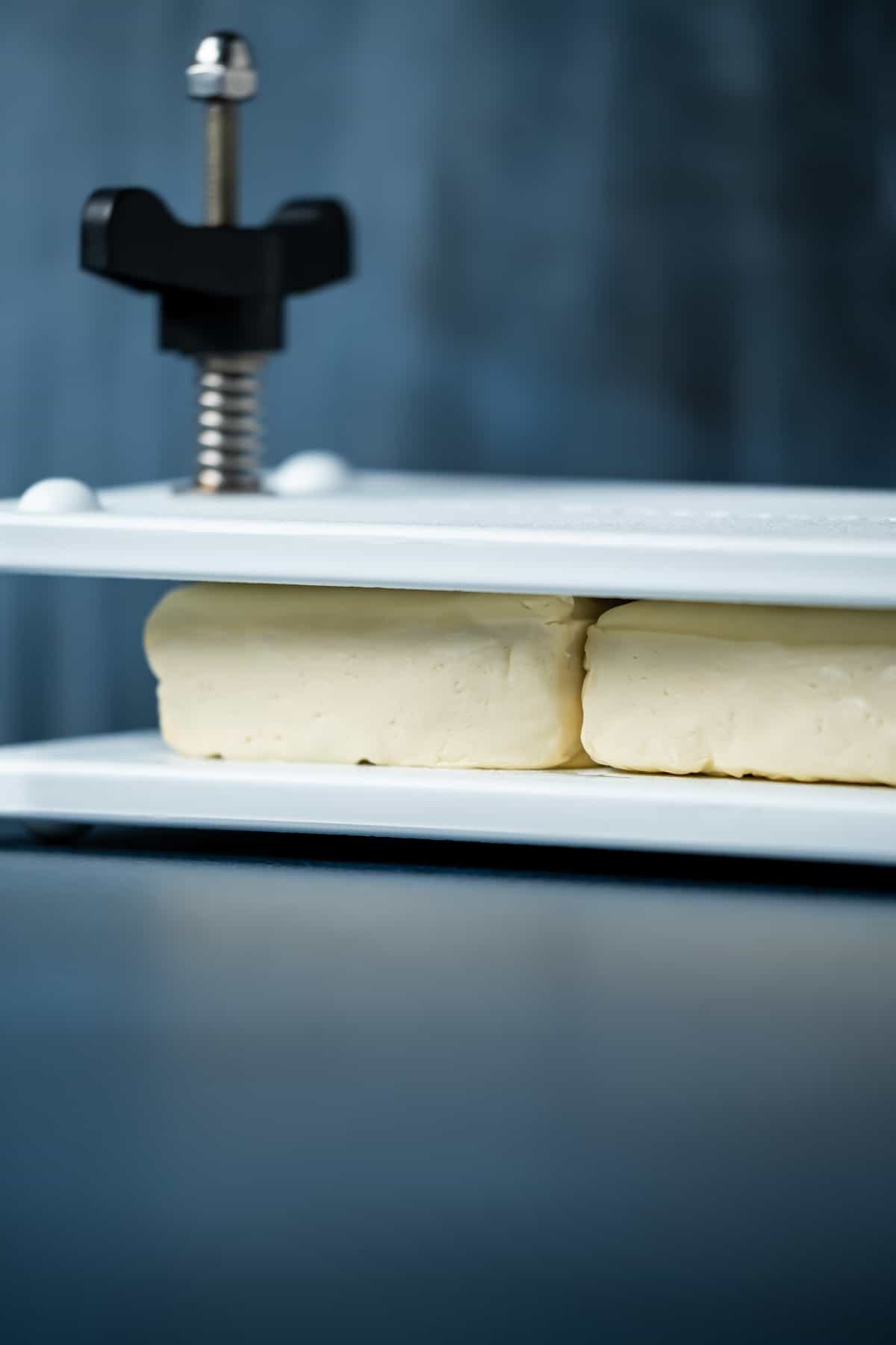 Photo of two blocks of tofu pressing in a tofu press.