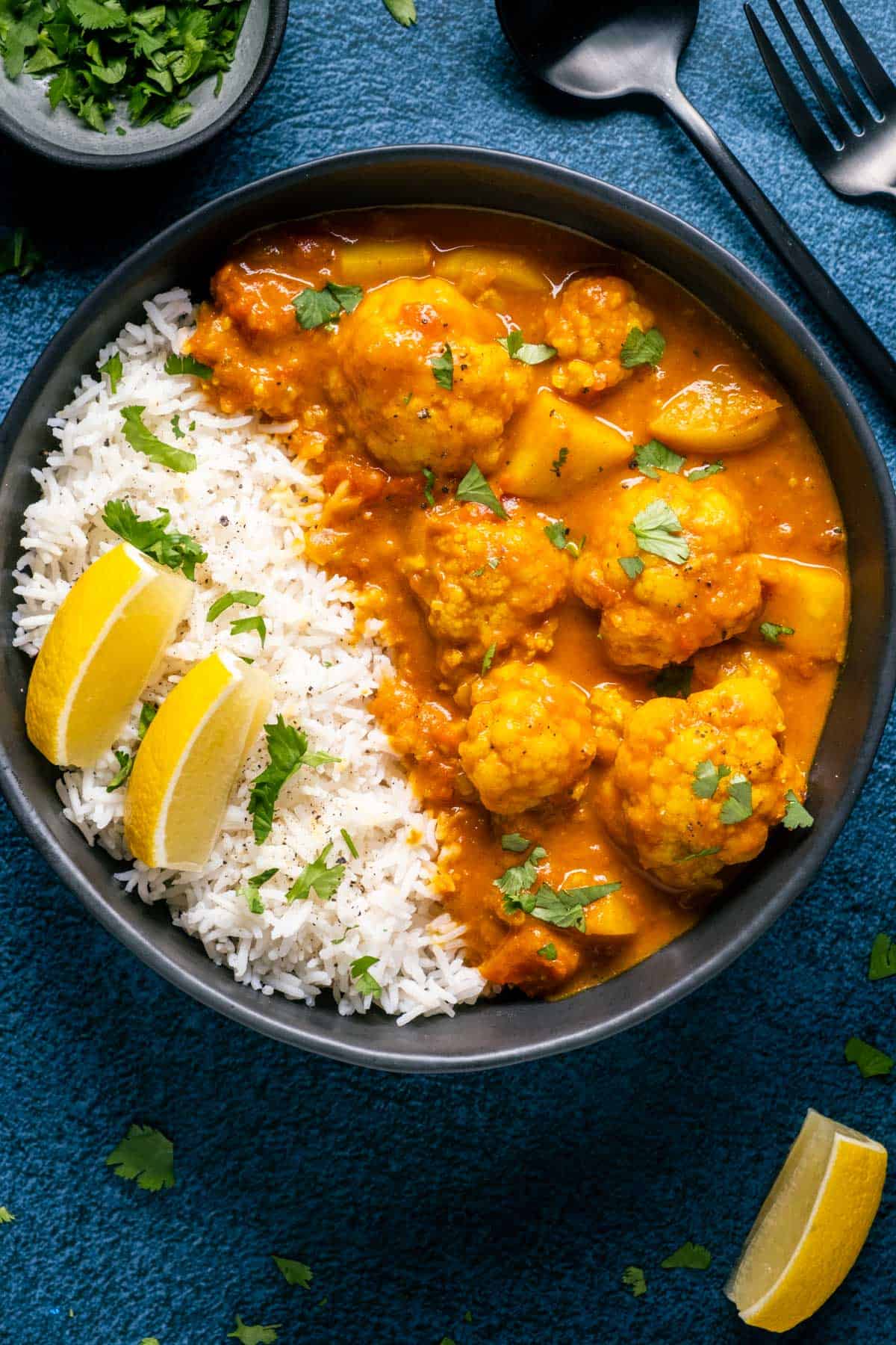 Vegan cauliflower curry with rice and lemon wedges in a black bowl. 