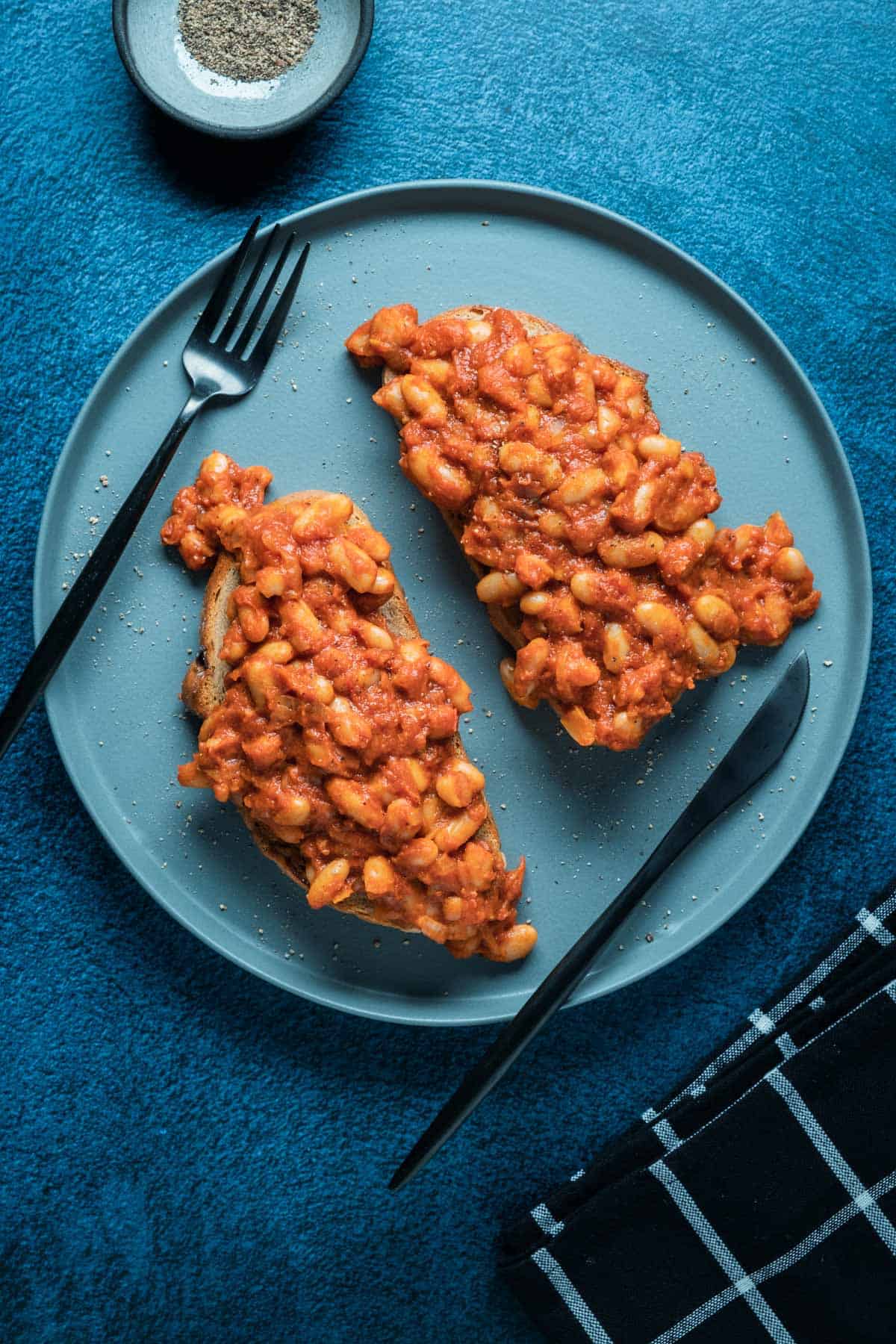Two slices of toast topped with vegan baked beans on a blue plate. 