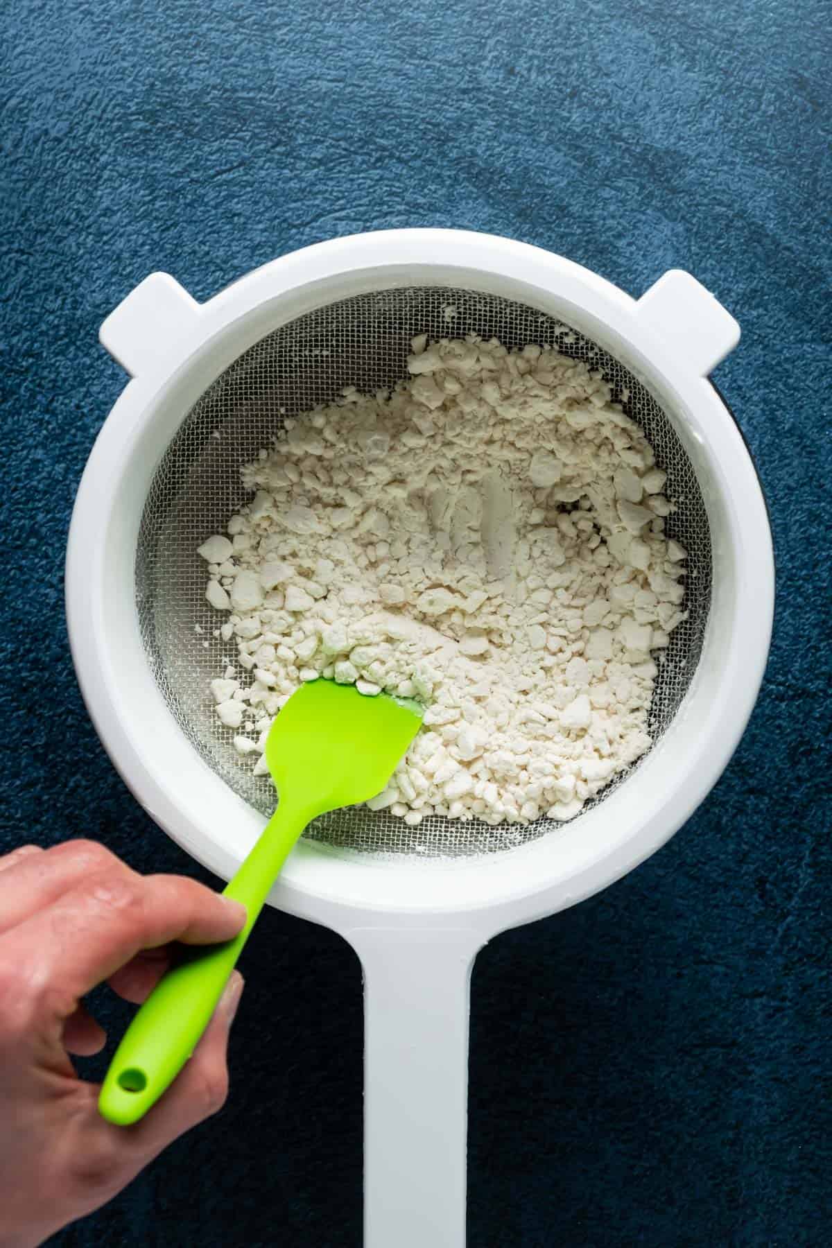Sifting flour in a sieve over a bowl.