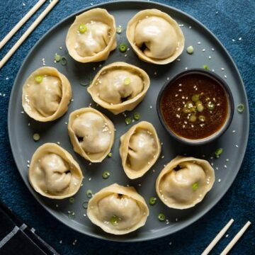 Dumplings on a plate with dipping sauce and topped with chopped green onions.