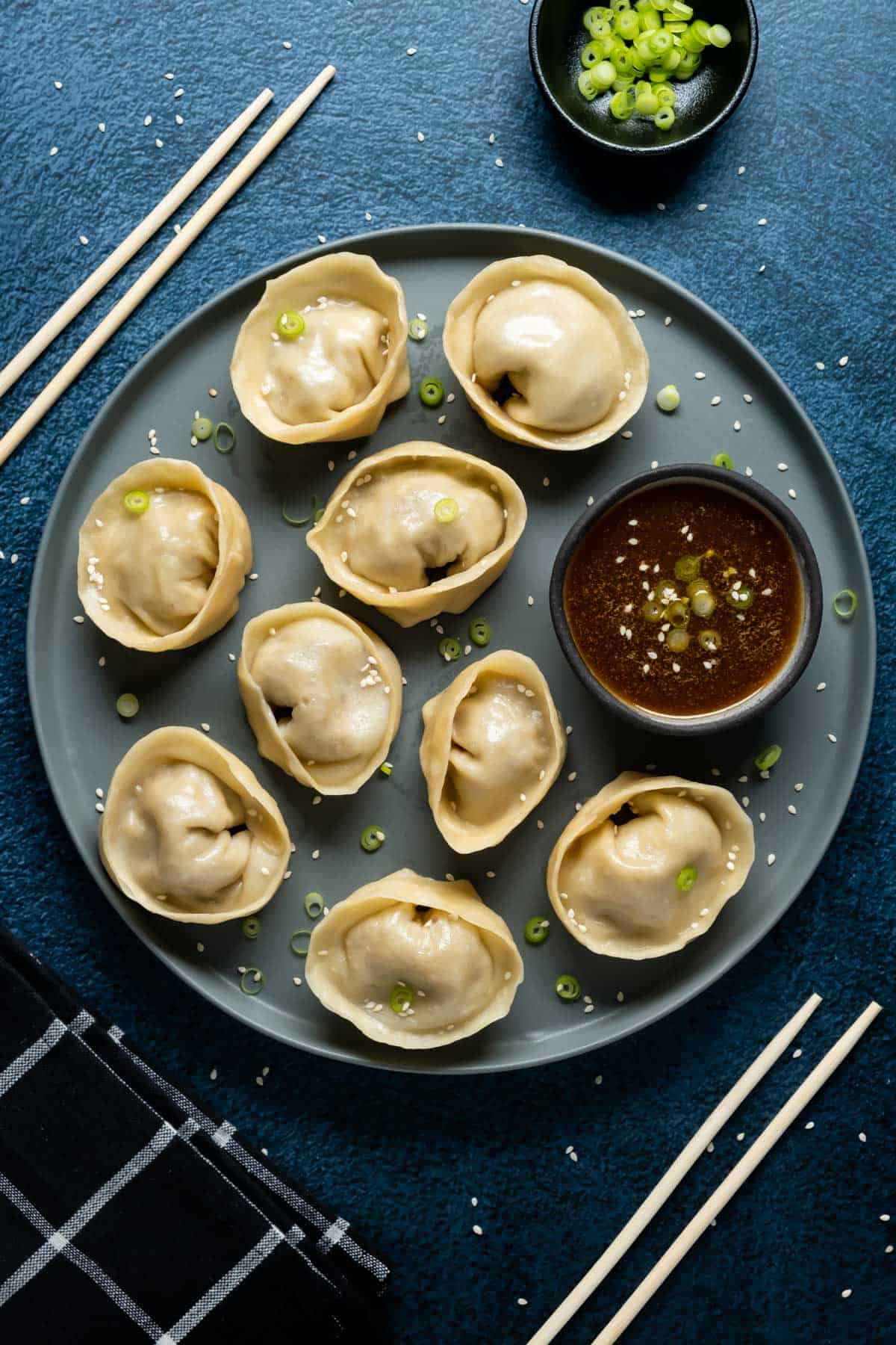Dumplings on a plate with dipping sauce and topped with chopped green onions. 