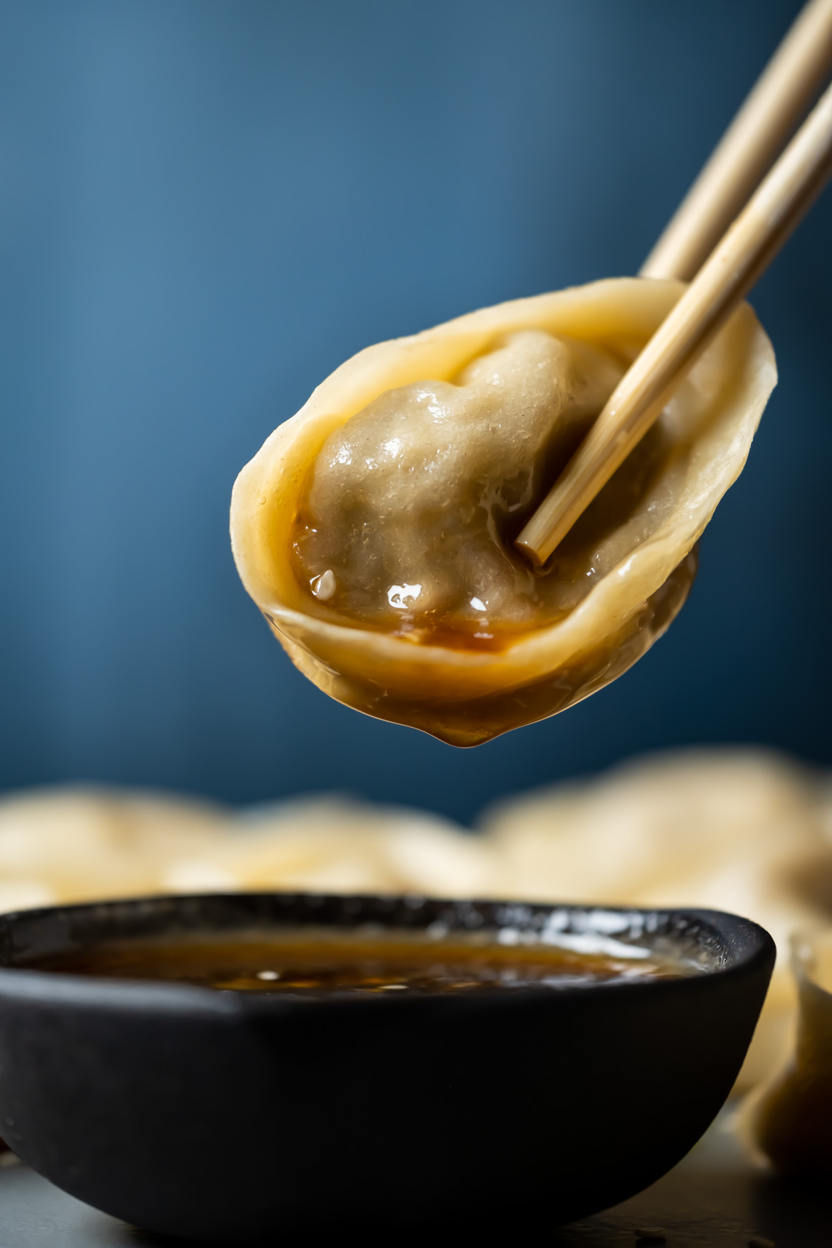 Chopsticks holding a dumpling above a bowl of dipping sauce.