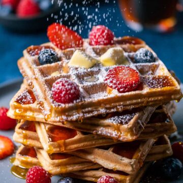 Powdered sugar sprinkling down over a stack of waffles.