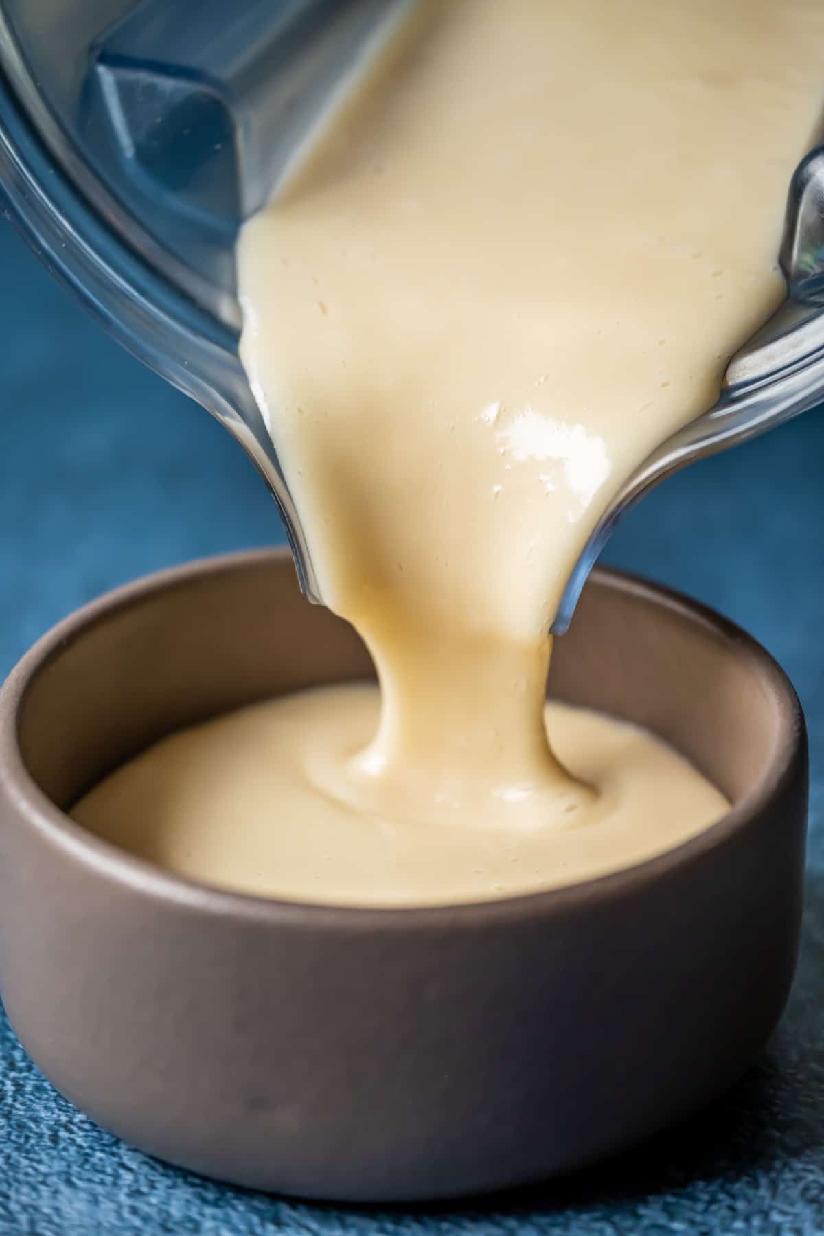 Vegan condensed milk pouring from a blender jug into a bowl.