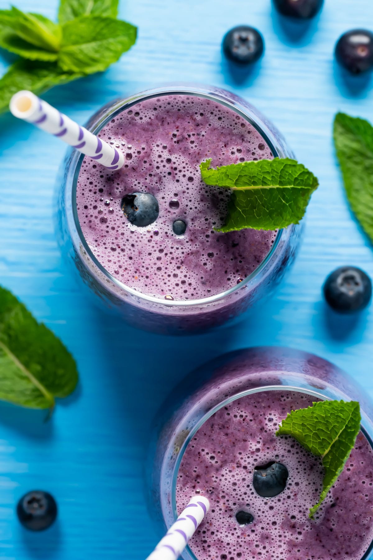 Blueberry smoothies in glasses topped with blueberries and fresh mint leaves.