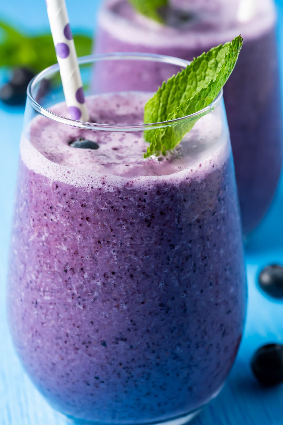 Blueberry smoothies in glasses with straws and fresh mint leaves. 