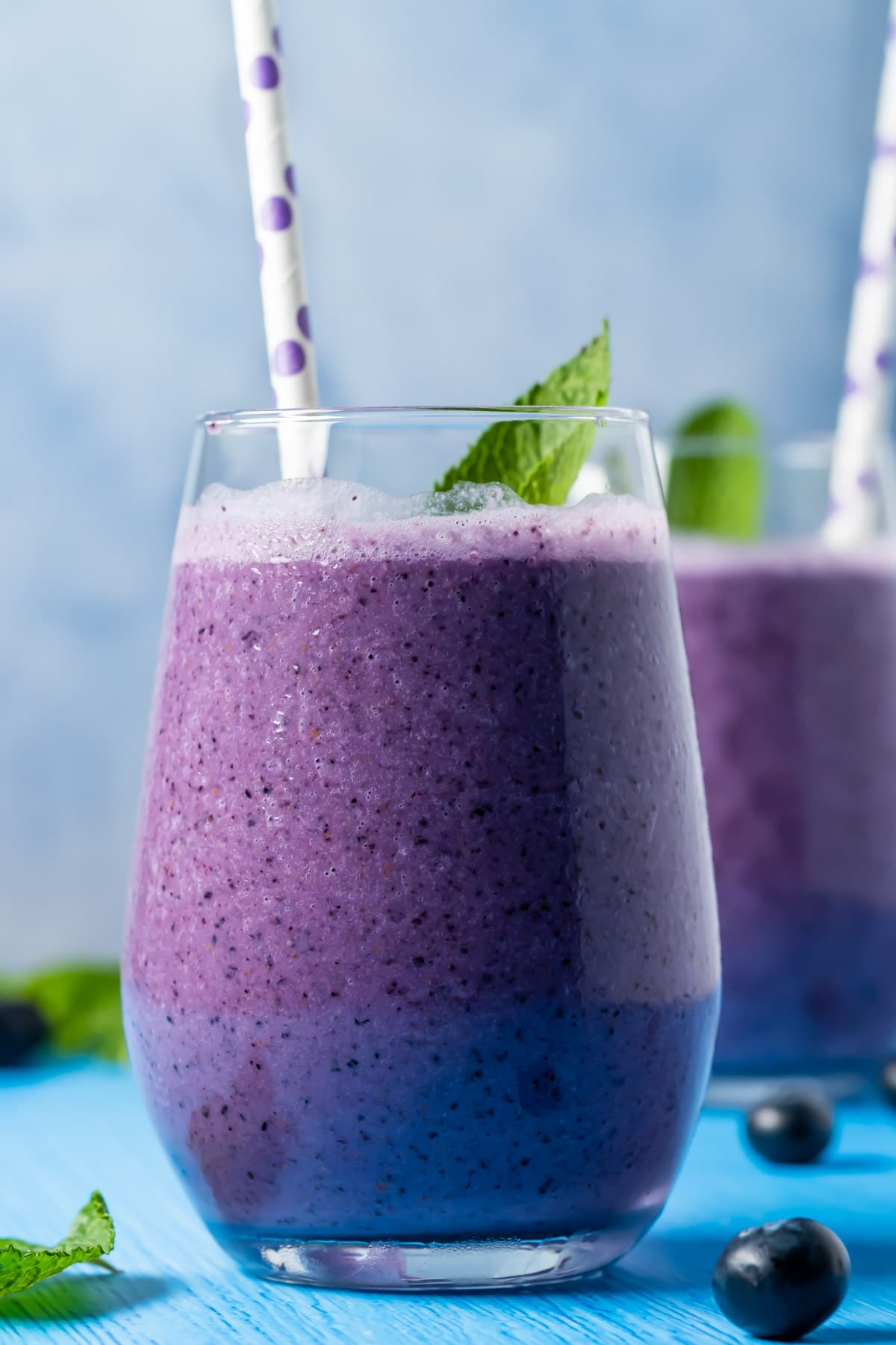 Blueberry smoothies in glasses with straws and fresh mint leaves.