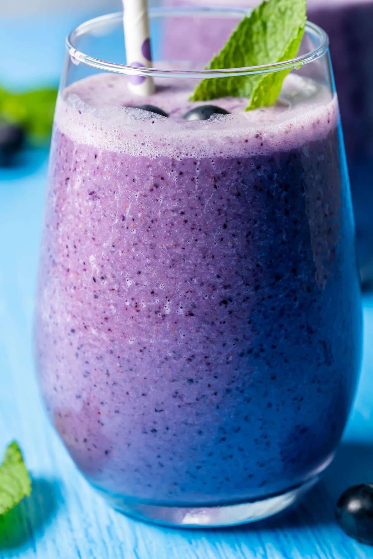 Blueberry smoothie in a glass with a straw and fresh mint leaves.