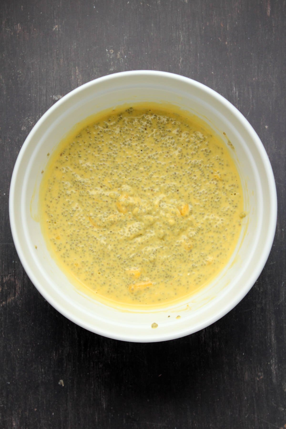 Coconut milk, chia seeds, maple syrup and mango purée mixed together in a mixing bowl.