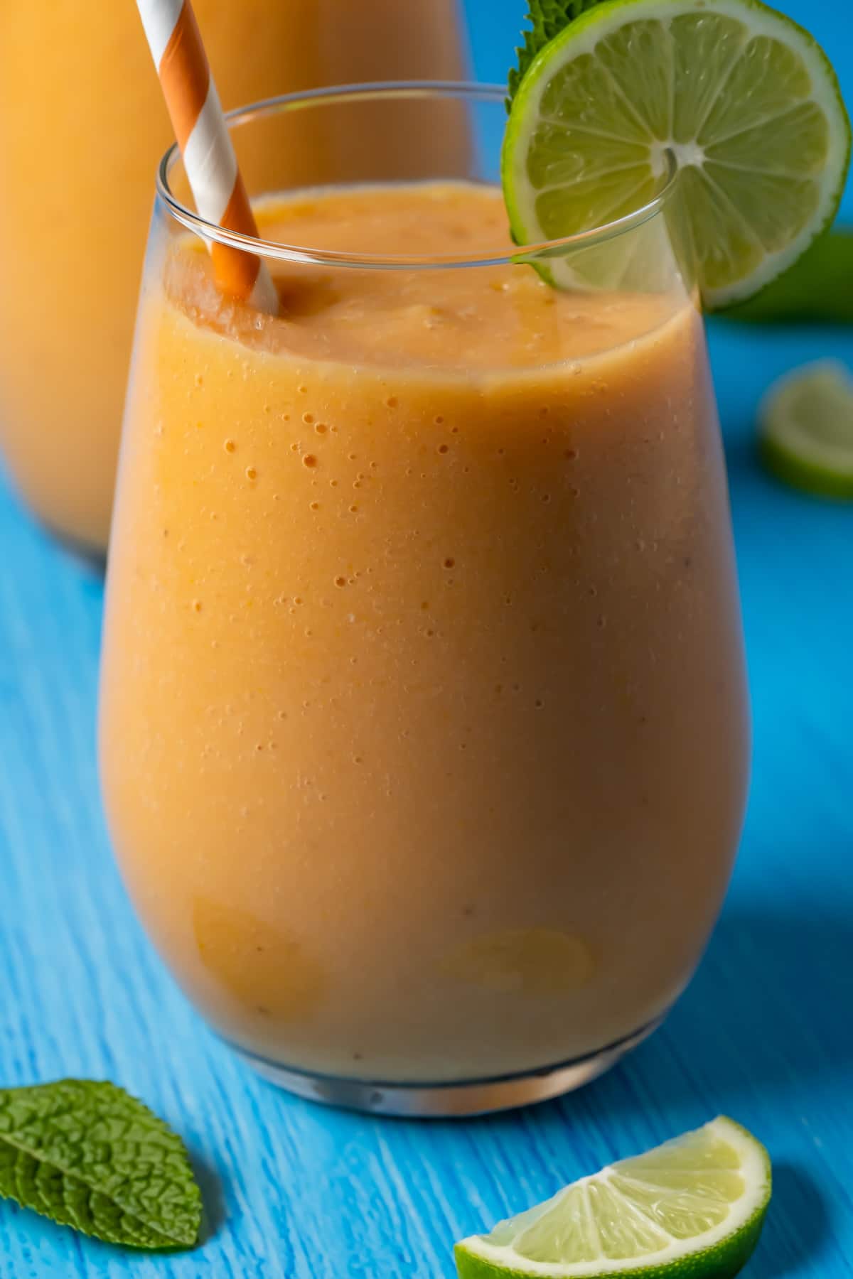 Papaya smoothie in glasses with mint leaves, fresh lime and striped straws. 