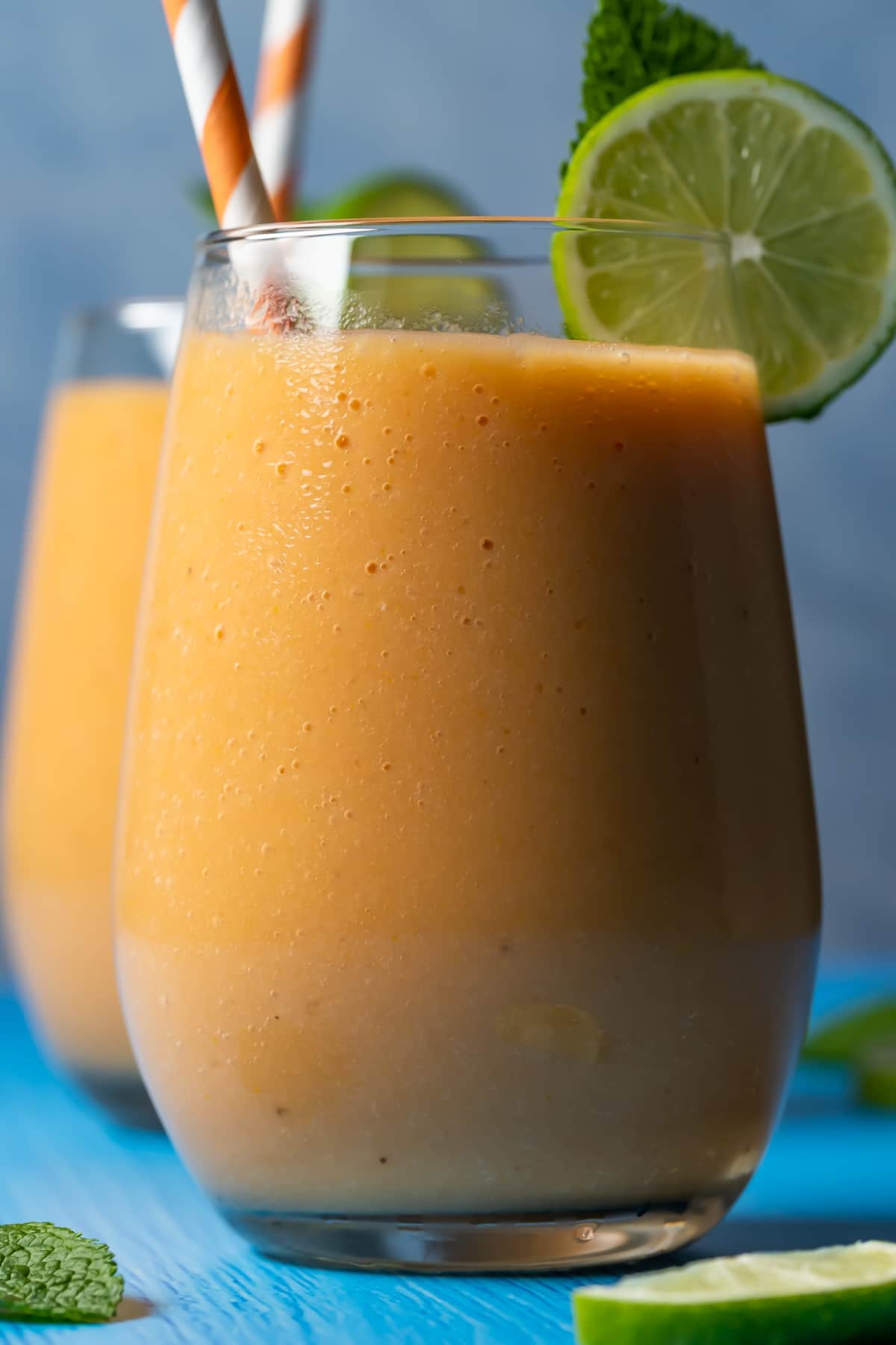 Papaya smoothie in glasses with mint leaves, fresh lime and striped straws.