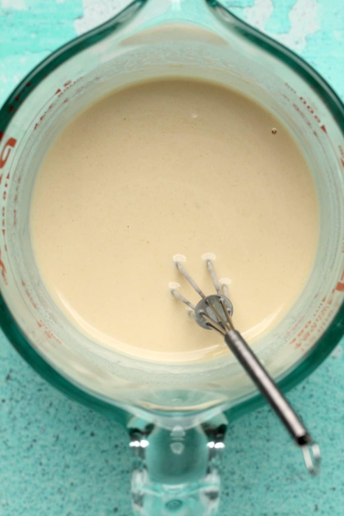 Tahini sauce in a measuring jug with a whisk.