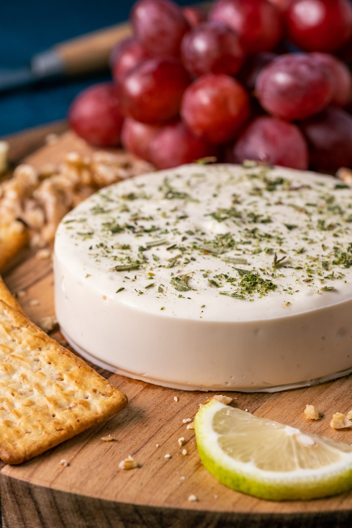 Vegan goat cheese on a wooden board with crackers, nuts and grapes.