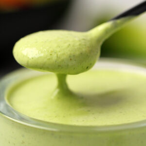 Vegan green goddess dressing in a glass jar with a spoon.
