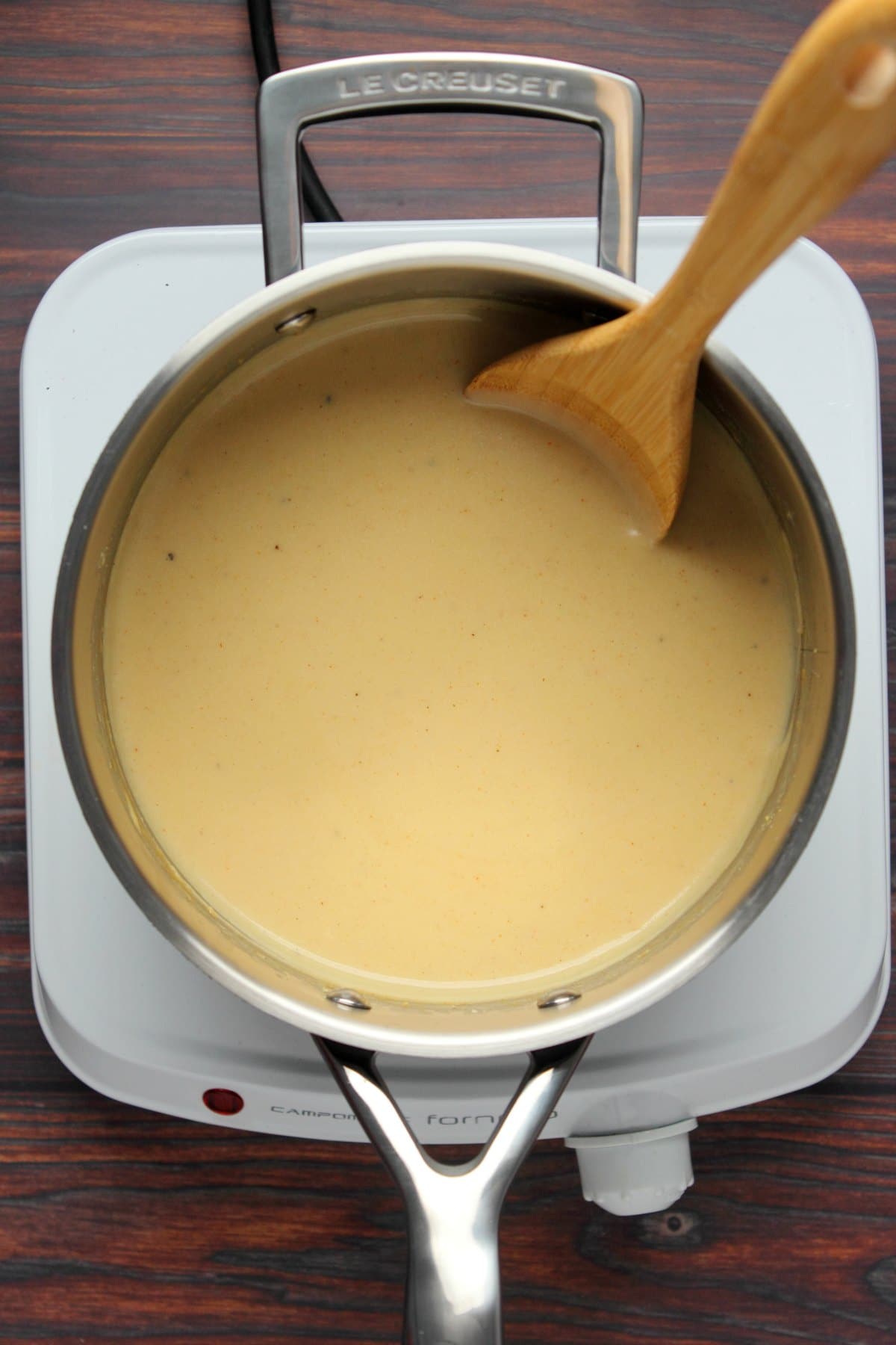 Vegan cheese sauce in a saucepan with a wooden spoon.