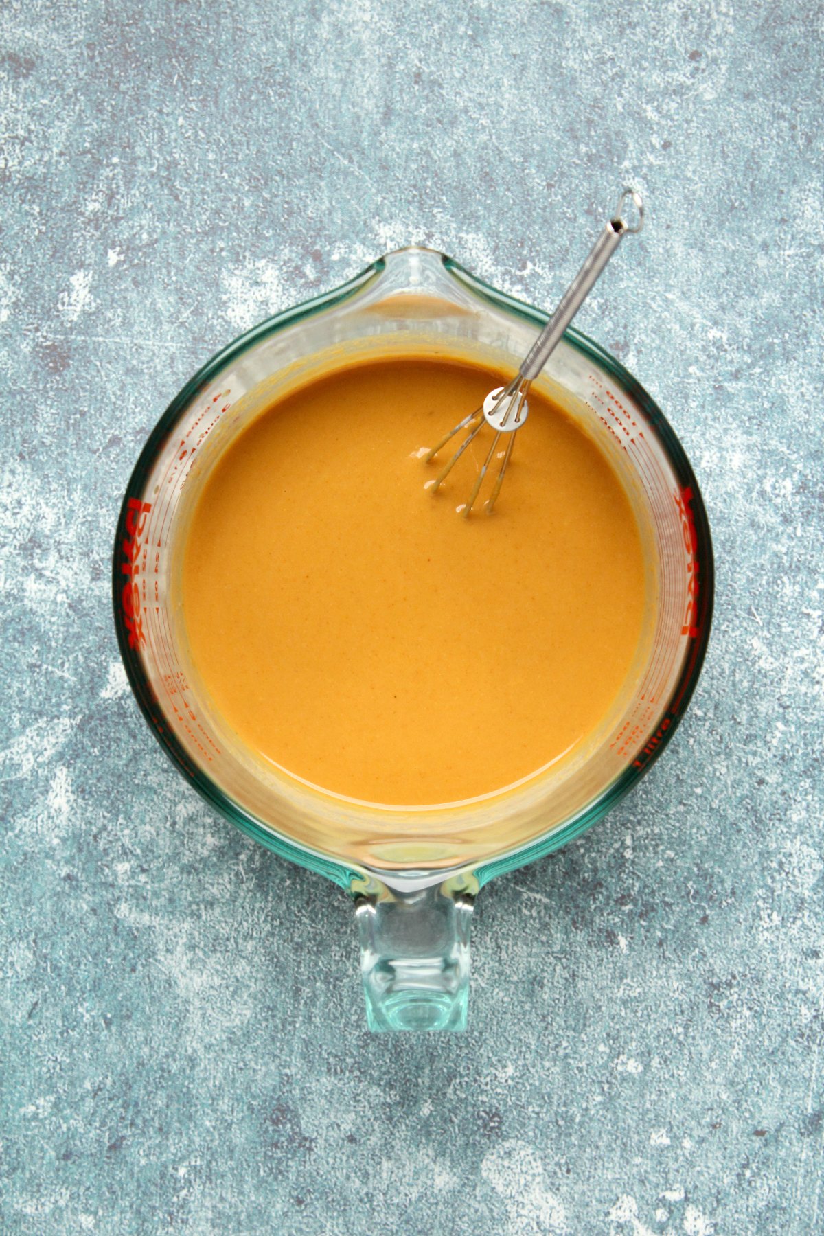 Vegan peanut sauce in a measuring jug with a whisk.
